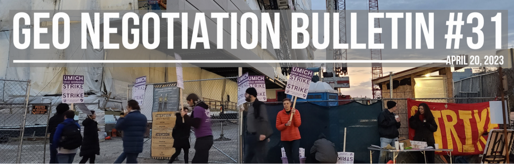 A circular picket line in front of a construction site. There is a large banner that says "STRIKE" on the right