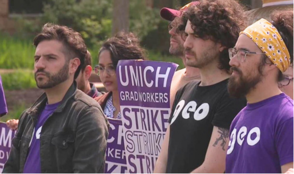 5 people in GEO shirts sternly looking out while holding a strike sign